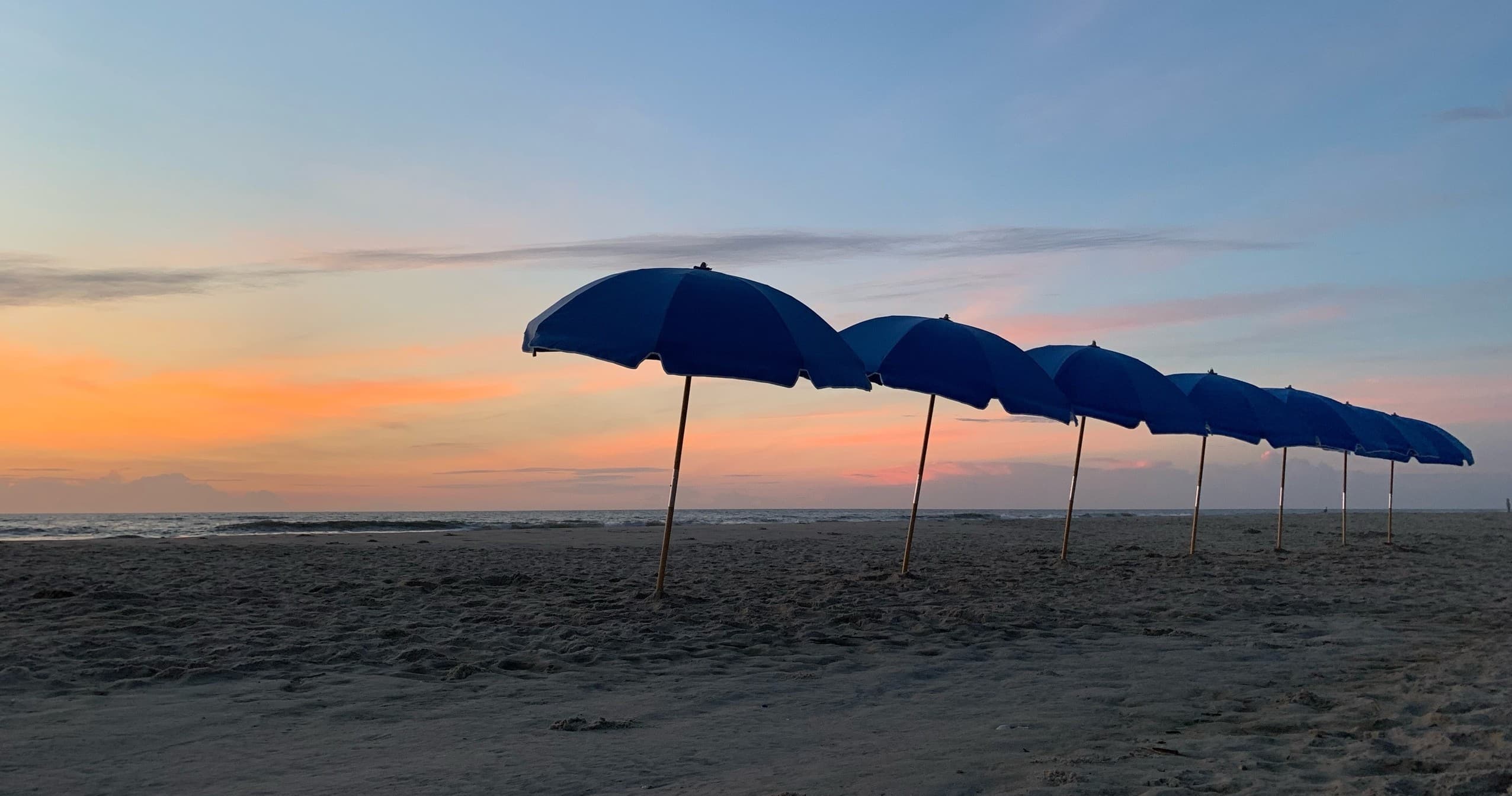 Line of blue beach umbrellas along the shoreline at dusk