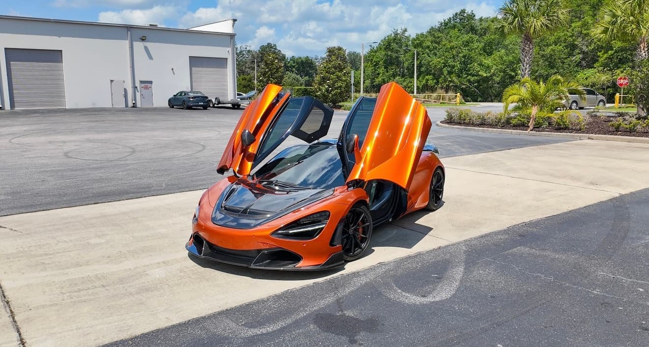 Orange McLaren sports car with butterfly doors in sunny parking lot