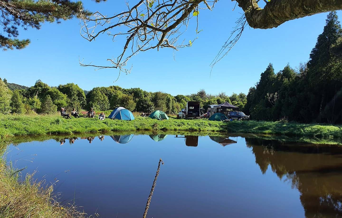 Calm pond reflecting tents and trees at scenic campsite