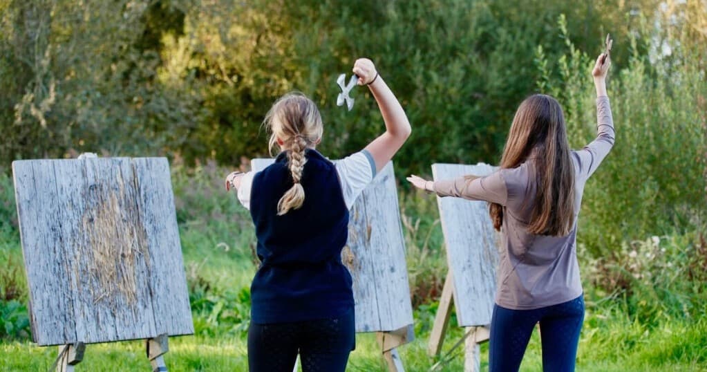 Two people axe throwing at wooden targets in woodland clearing