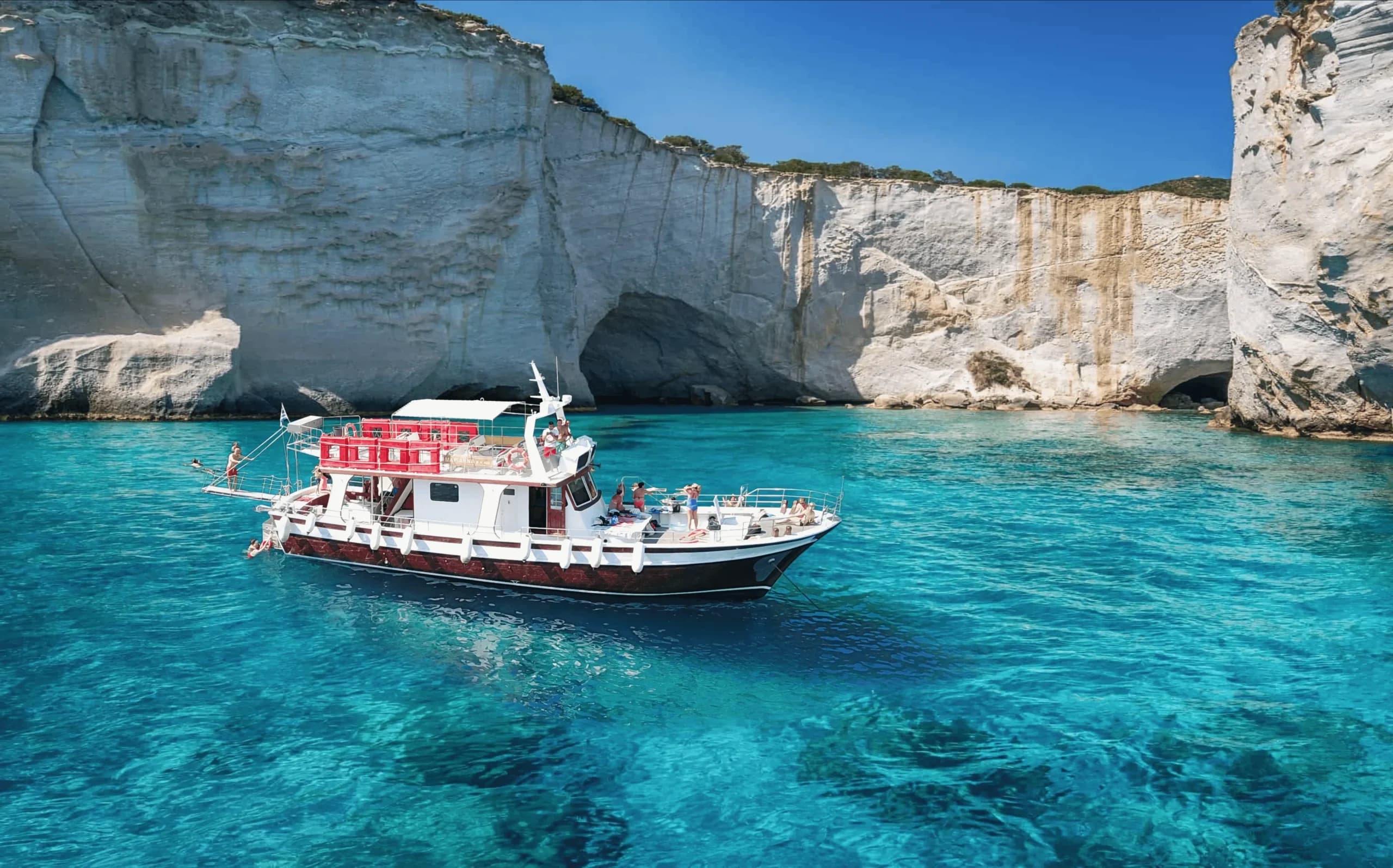 Tour boat cruising turquoise waters near white limestone cliffs, Milos