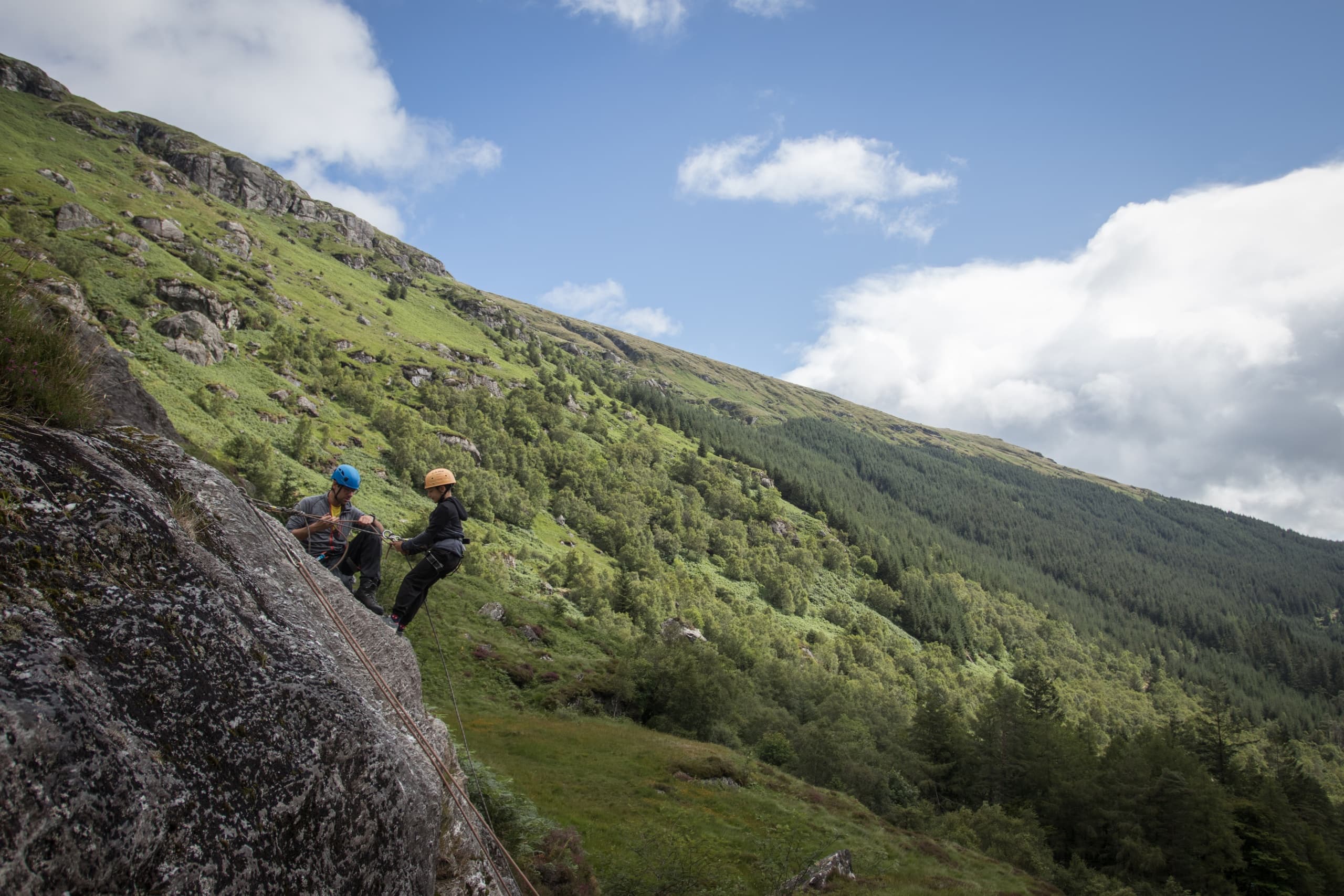 Hikers scrambling along green glen ridge with sweeping vistas
