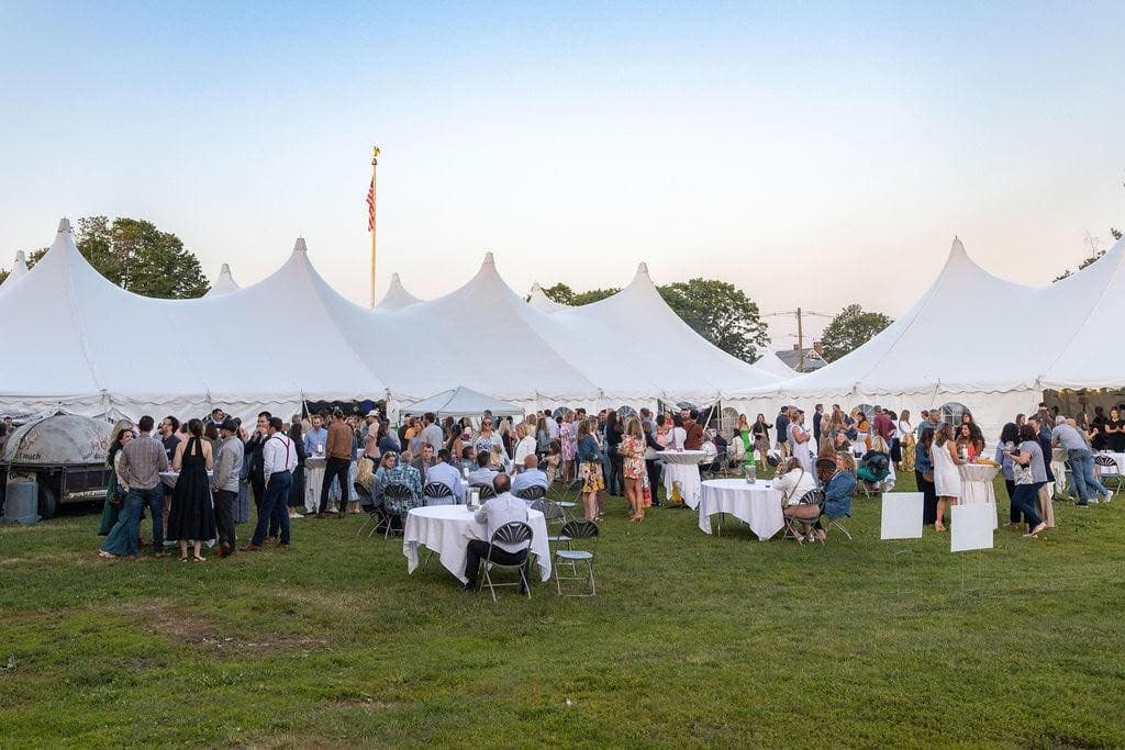 Crowd gathering under large white festival tents on grassy field