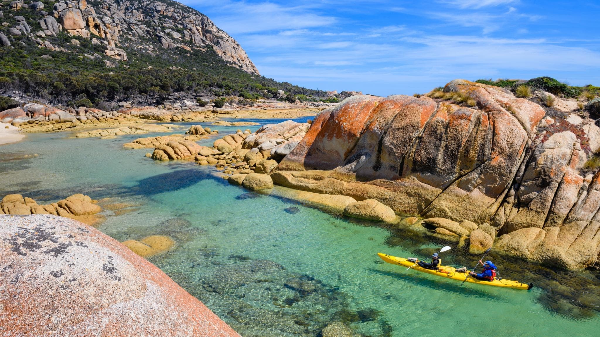 Single kayaker exploring crystal clear rocky coastal cove