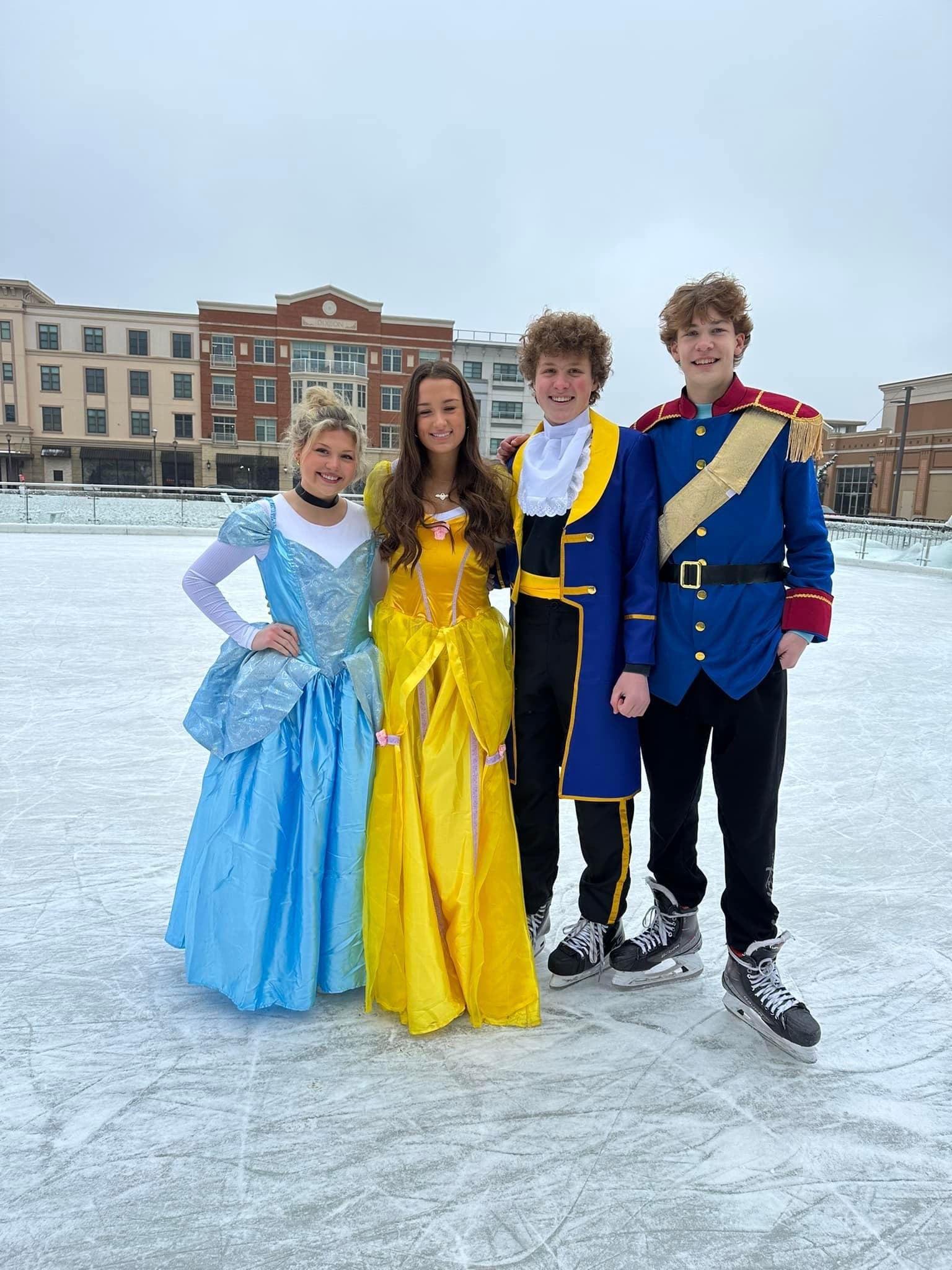 Costumed princesses and prince posing on outdoor ice rink