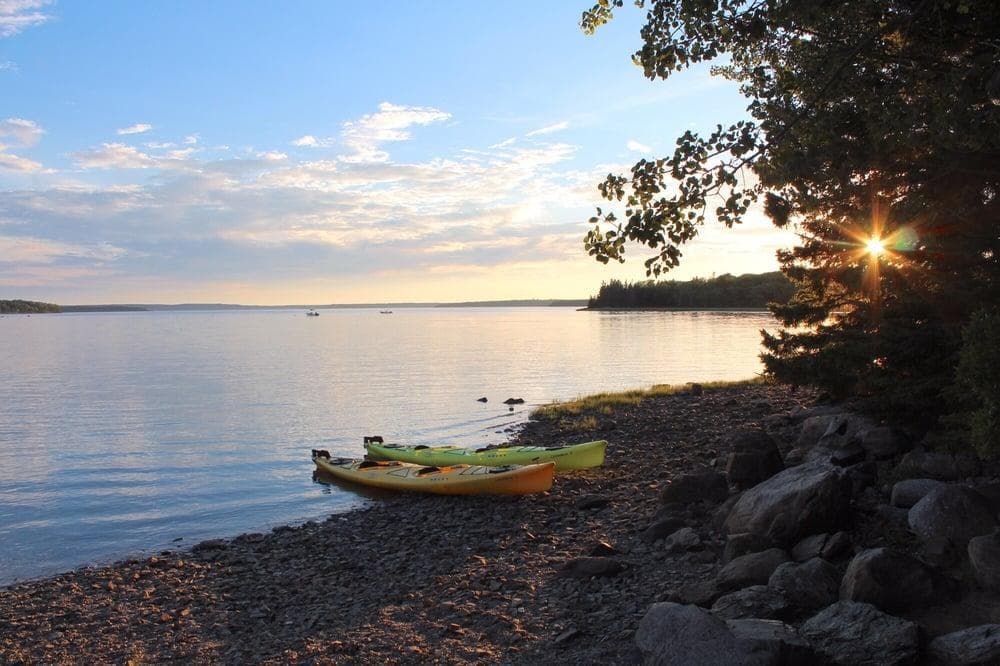 Kayak resting on rocky shoreline at golden sunset, peaceful bay