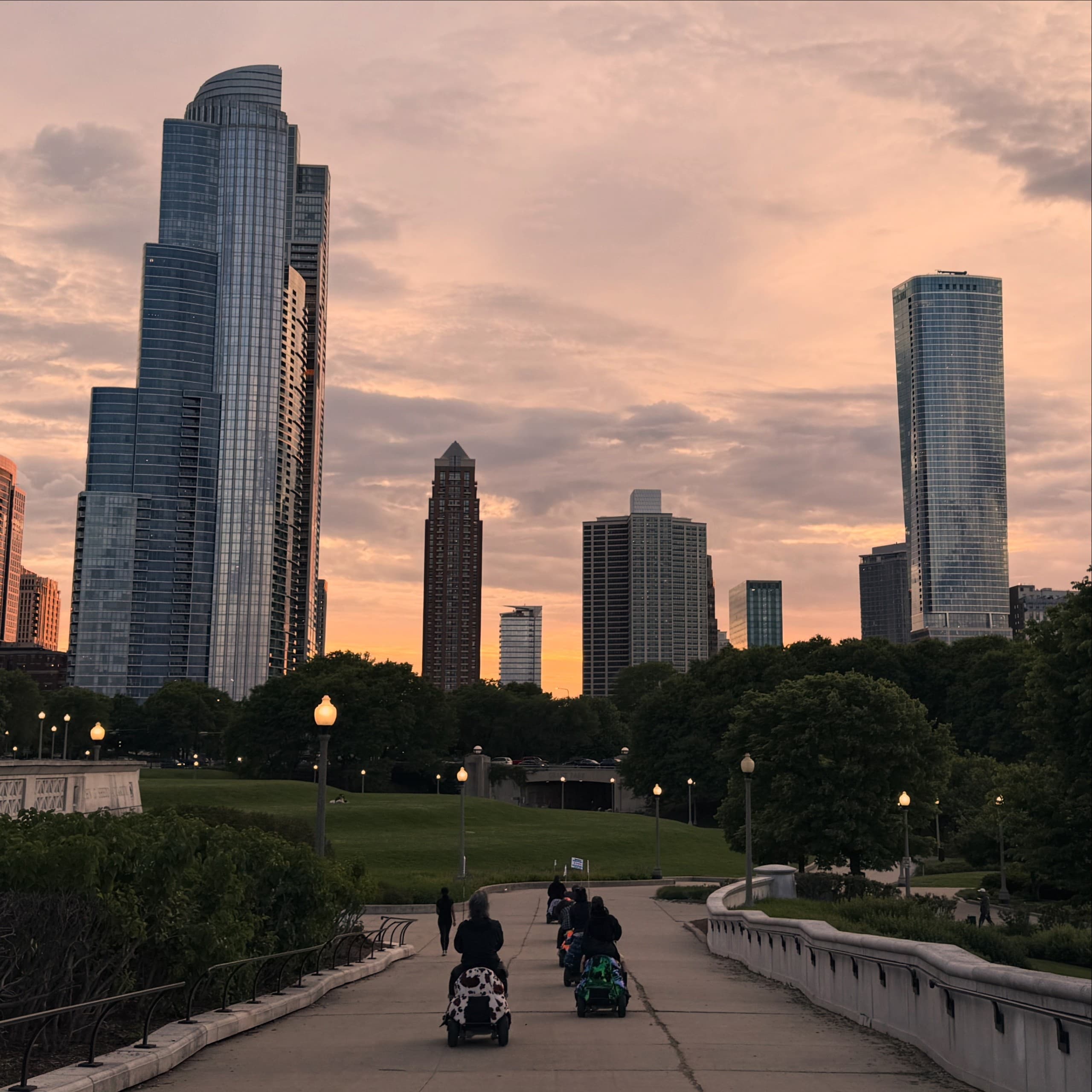 People on mobility scooters rolling toward Chicago skyline at sunset