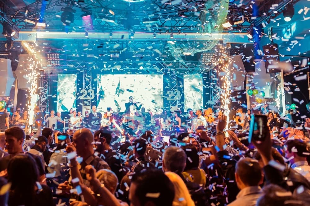 Crowd dancing at indoor nightclub concert with confetti and lights