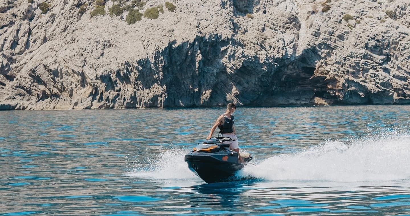 Jet ski cruising near rocky coastal cliffs in clear blue sea