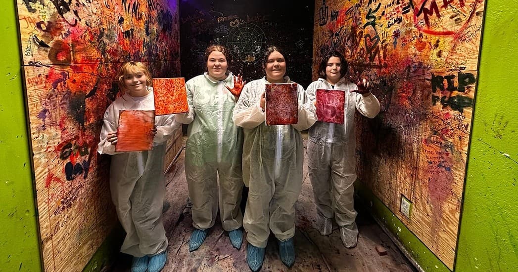 Four people in coveralls holding painted canvases in indoor smash room