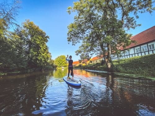 Stand-up paddleboarder cruising tree-lined canal near riverside houses