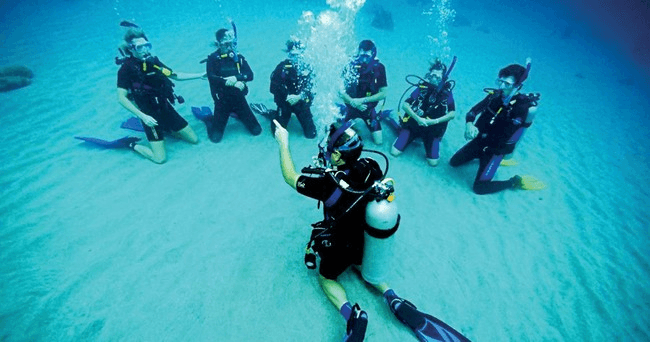 Group of scuba students kneeling on sandy seabed during training