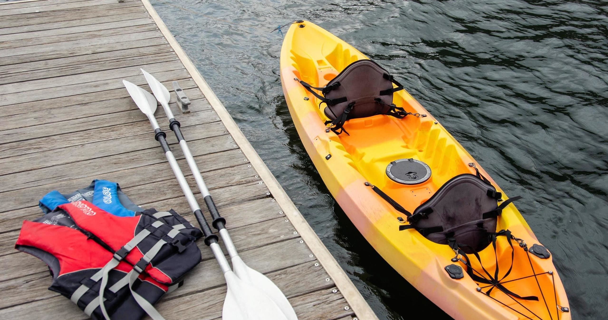 Two-person yellow kayak with paddles and life jackets on dock