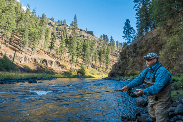 Angler fly fishing in forested river canyon during daytime