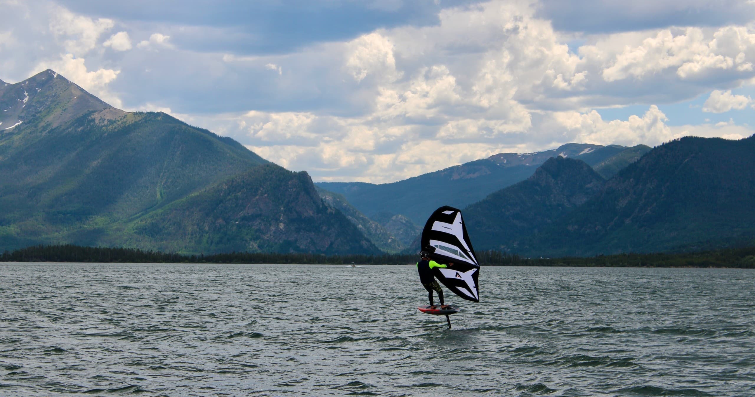 Wingfoiler gliding across alpine lake with mountain panorama