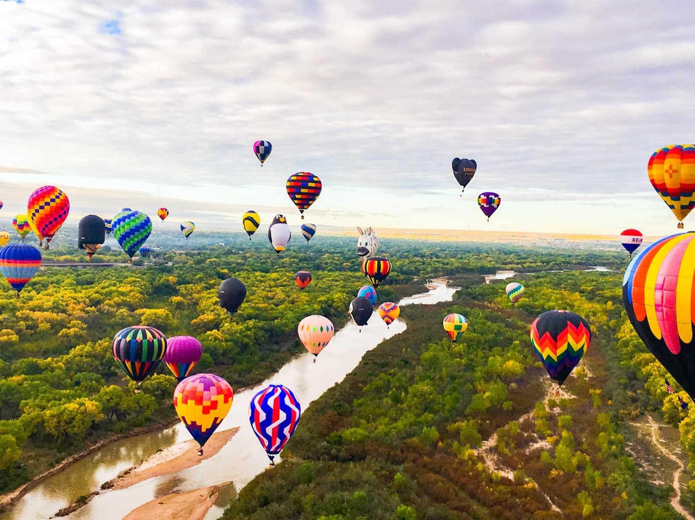 Hot air balloons drifting over river and green valley at sunrise