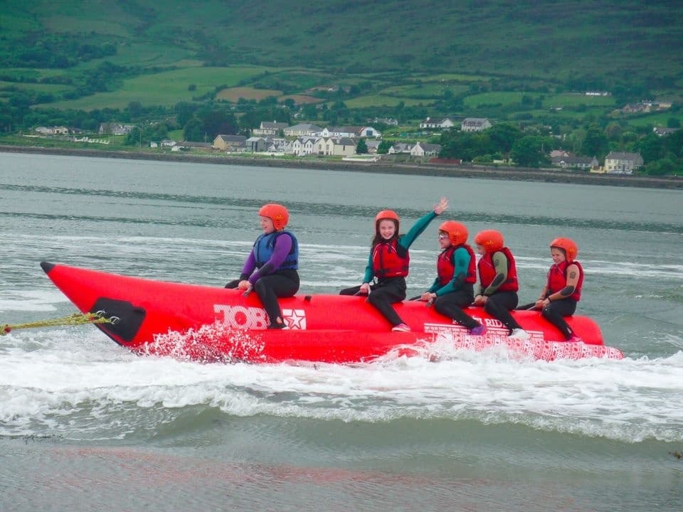 Riders on red inflatable banana boat speeding across bay