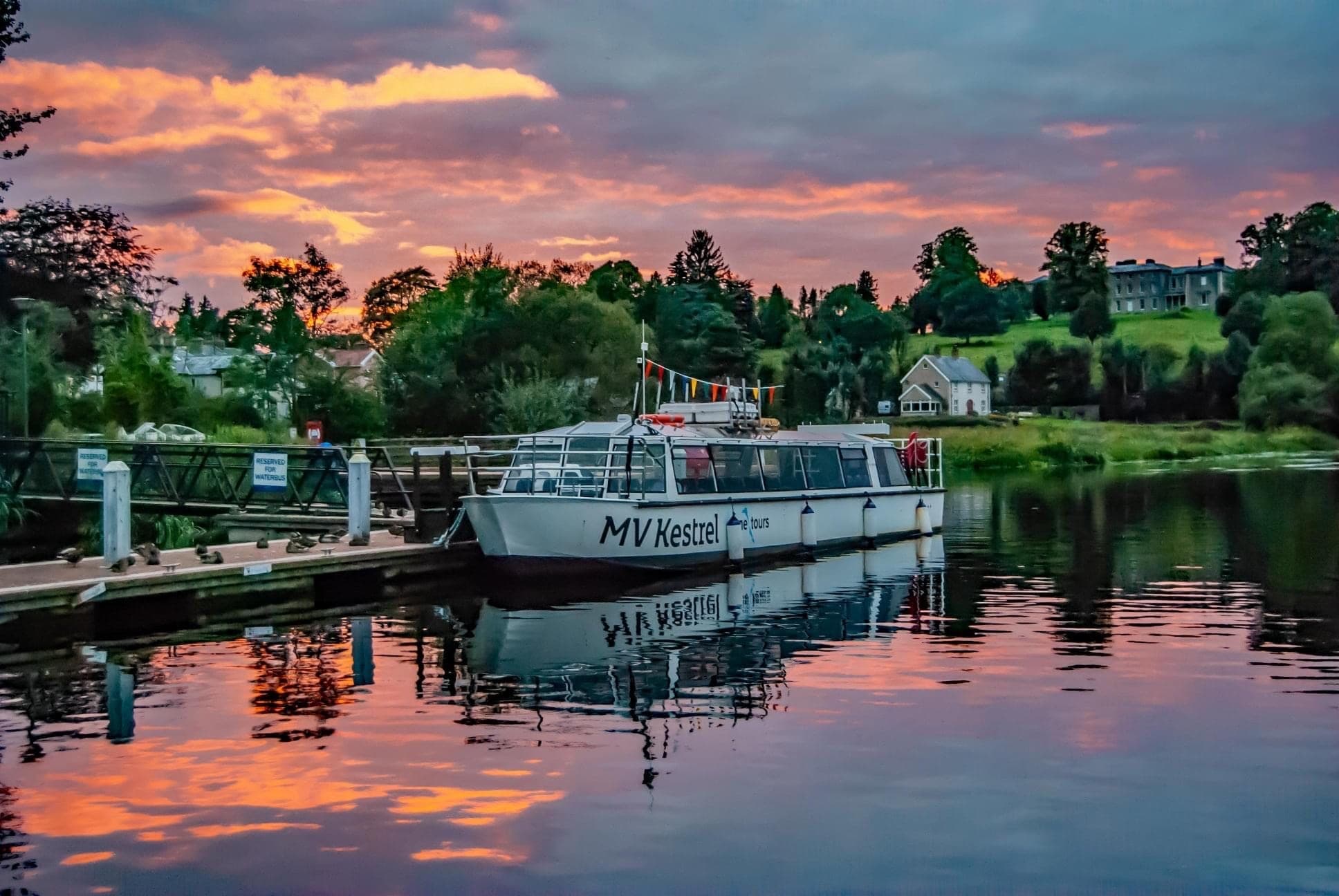 Sunset river cruise boat moored with colorful sky reflection