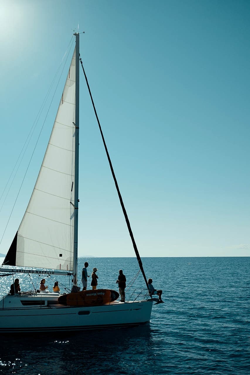 Tall sailboat with crew on calm sea under clear blue sky