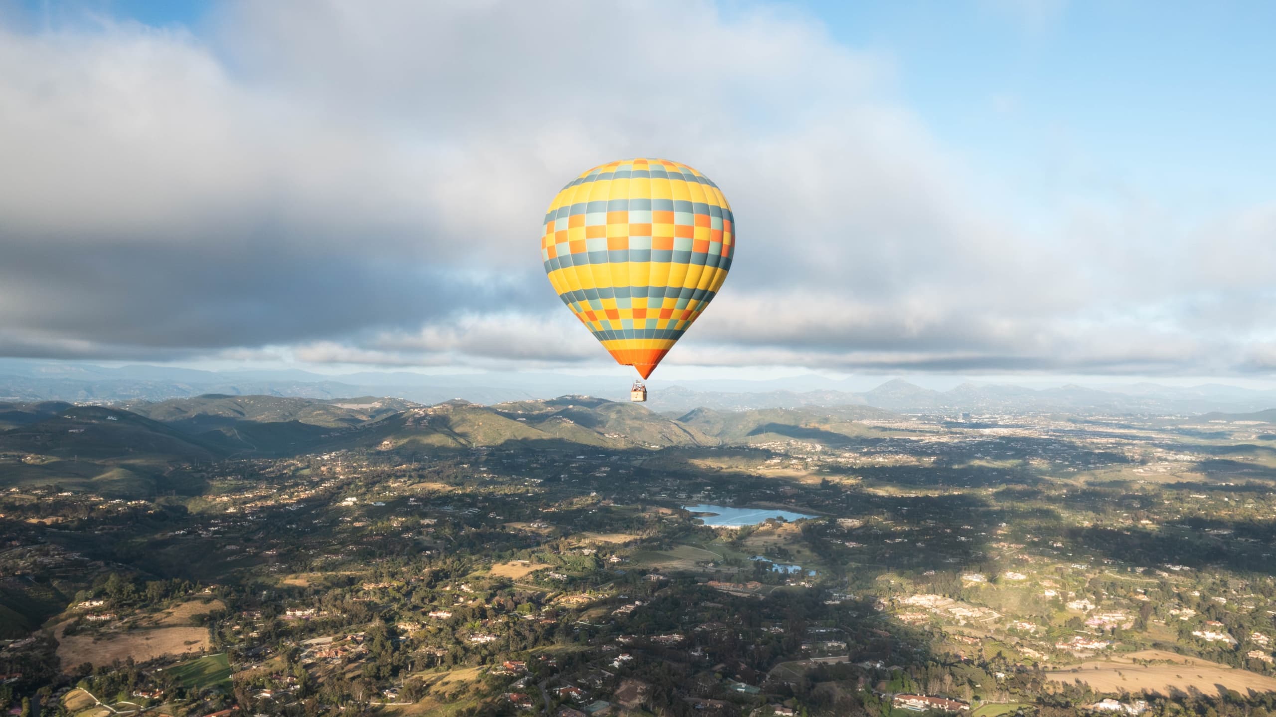 Single hot air balloon drifting over expansive valley landscape