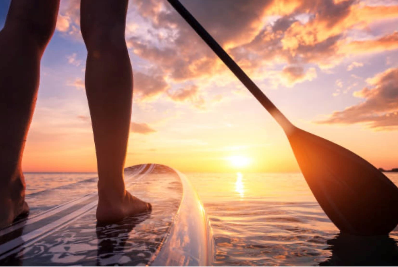 Standup paddleboarder paddling toward sunrise over ocean