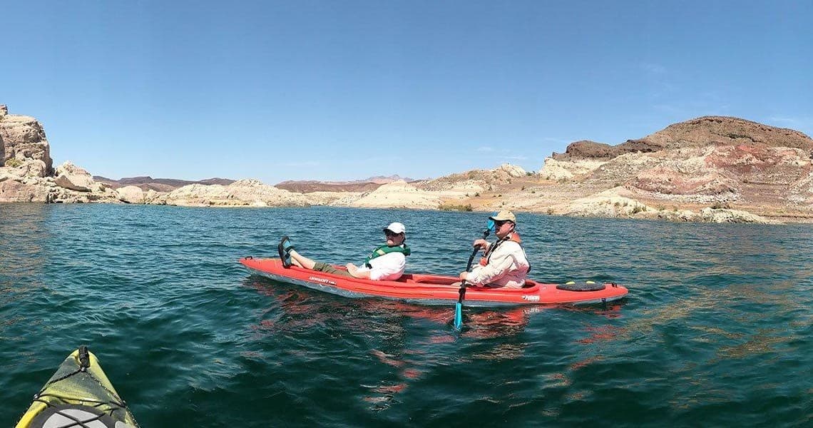 Two kayakers paddling on wide turquoise lake under blue sky