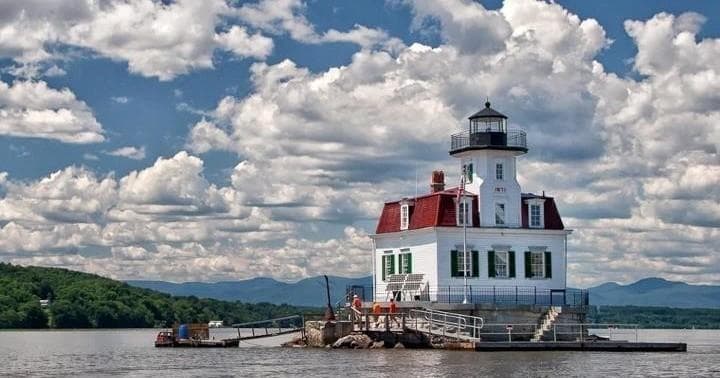 Historic lighthouse on river with dramatic clouds and pier