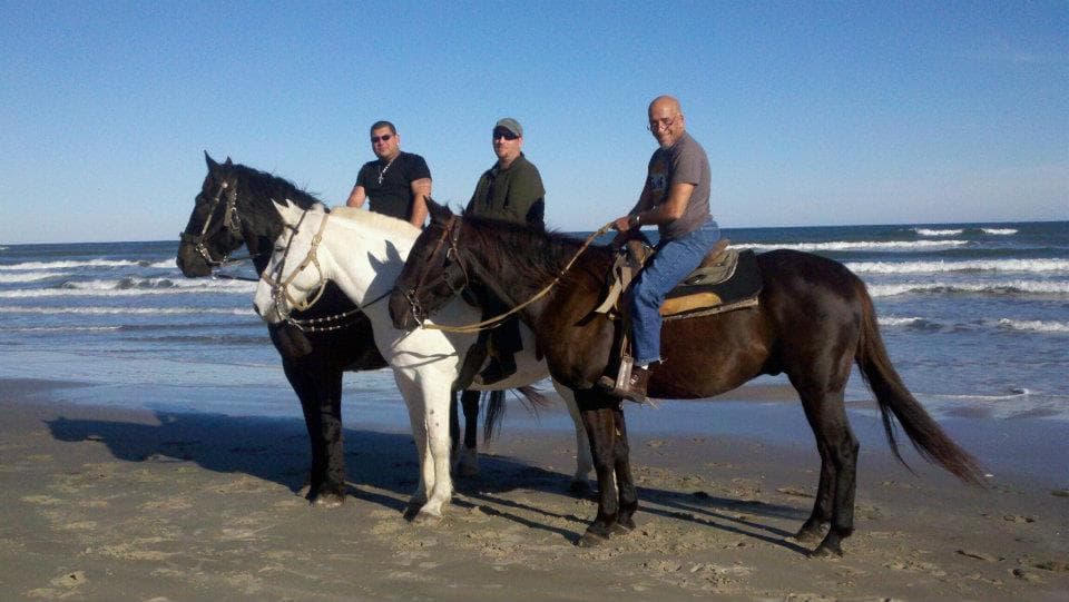 Three riders on horses standing on sandy Texas beach by waves