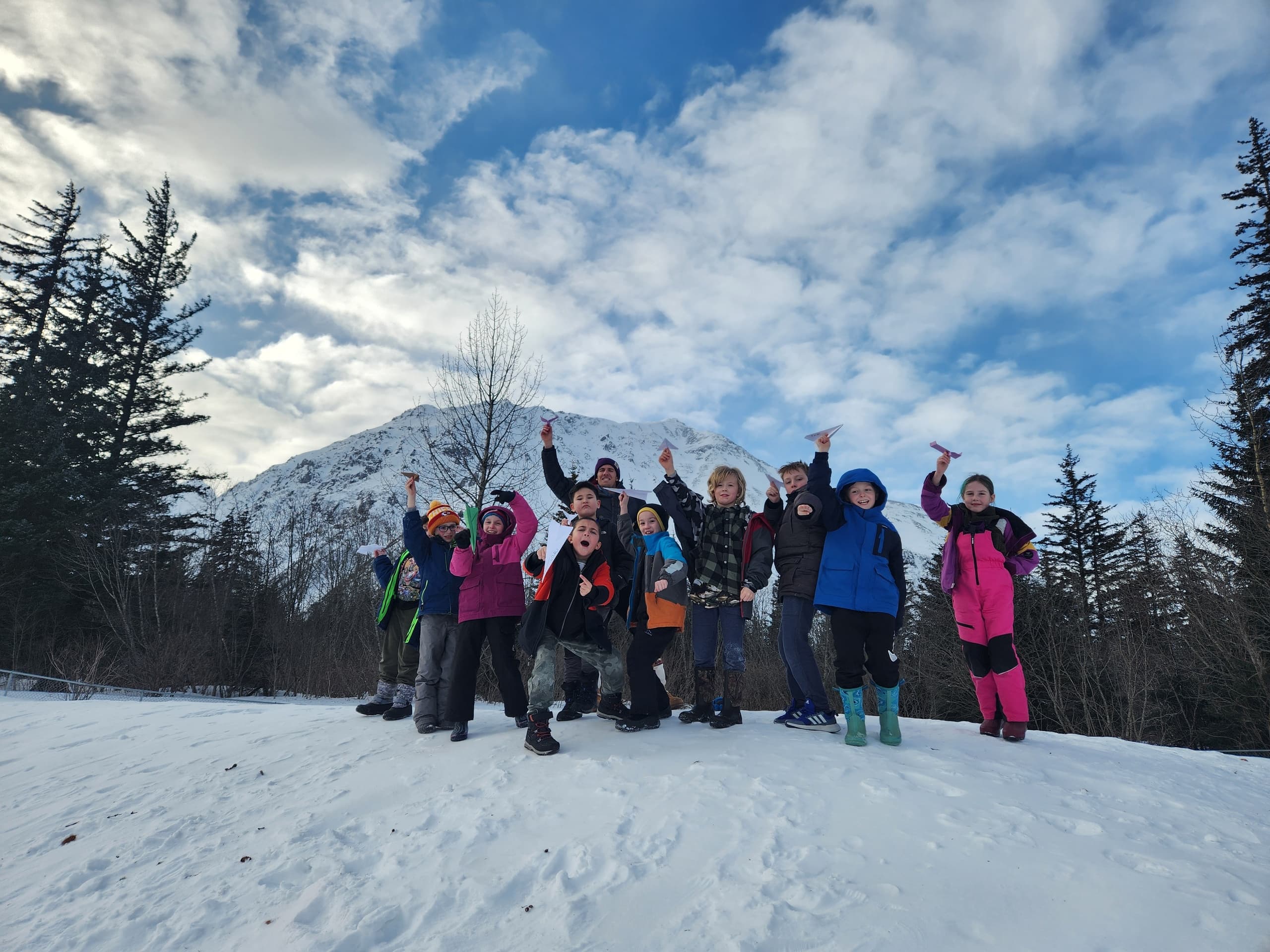 Group hiking and celebrating on snowy trail with mountain backdrop