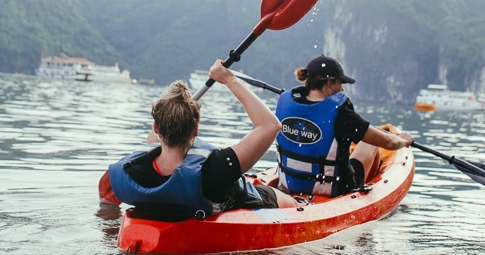 Two kayakers paddling in busy tourist bay with limestone cliffs