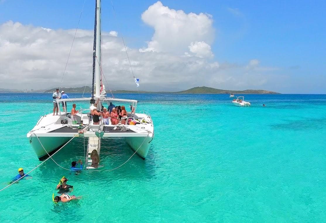 Catamaran cruising turquoise Caribbean waters with swimmers