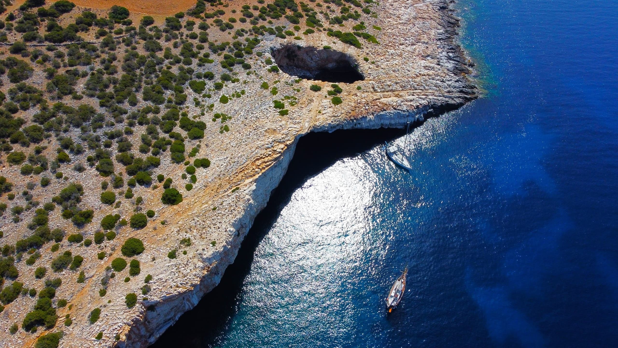 Coastal cliff with sea cave and small boat, dramatic aerial