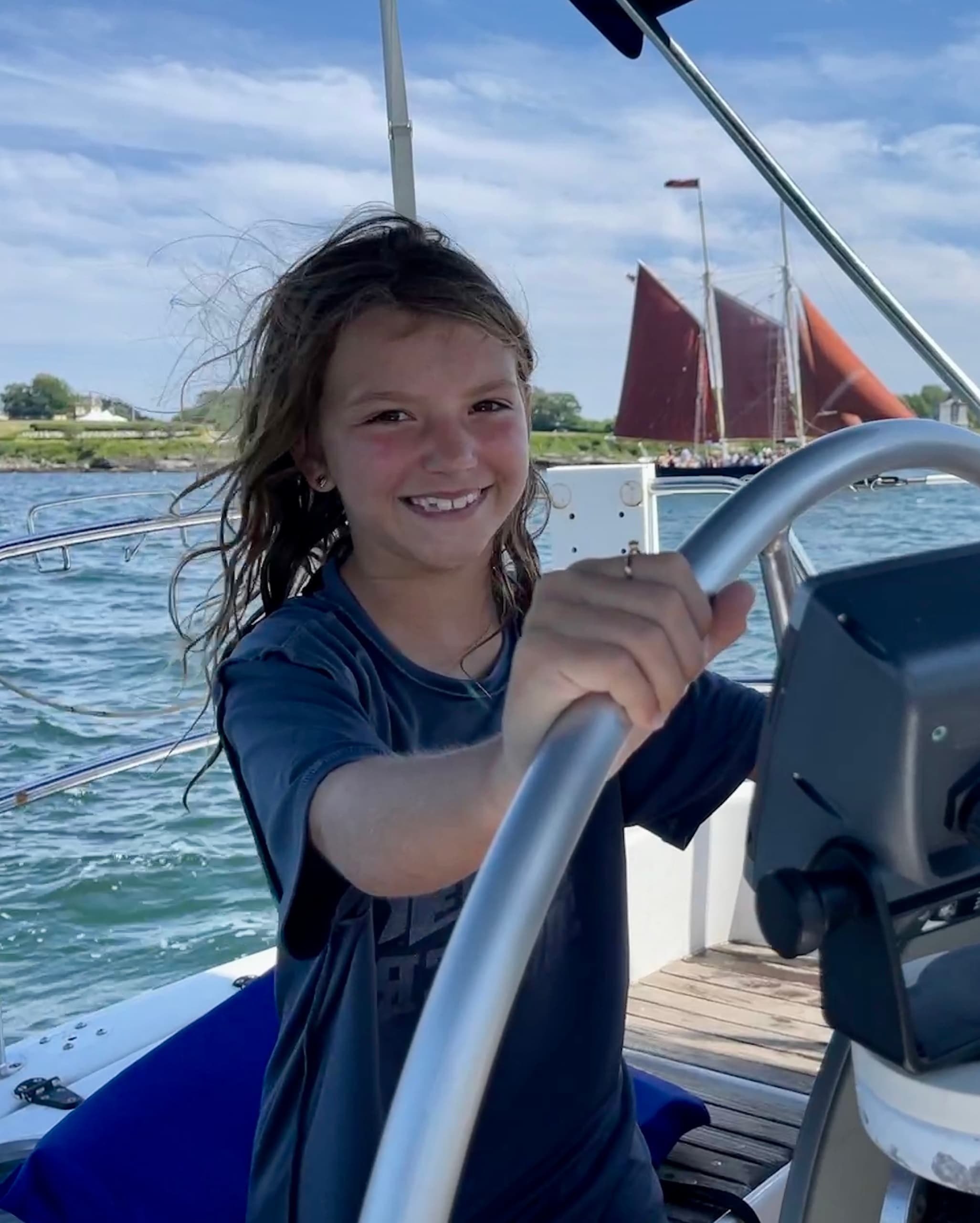 Smiling child steering sailboat helm on coastal waters