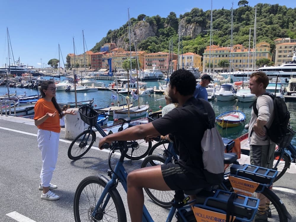 Bicyclists touring marina waterfront with yachts and coastal hills