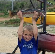 Child angler proudly holding rainbow trout on sandy lakeshore