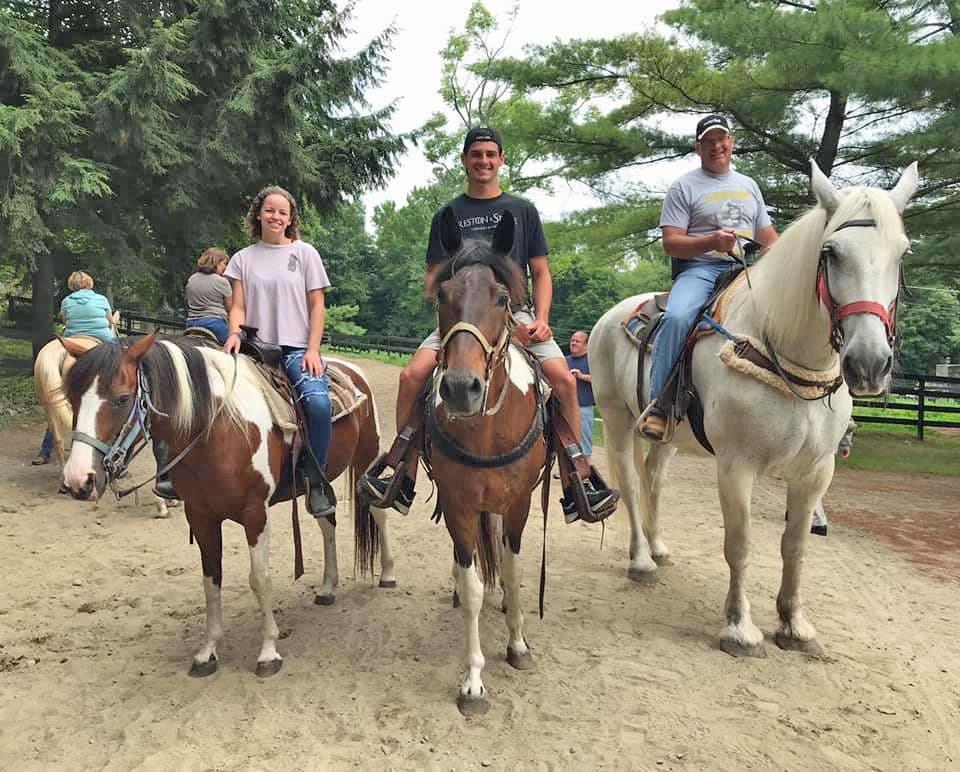 Horseback riders on a tree-lined dirt trail at riding stable