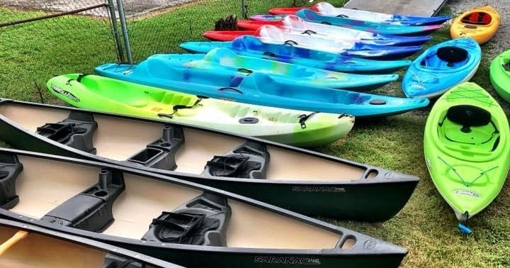 Colorful kayaks and canoes lined on grass, rental fleet ready