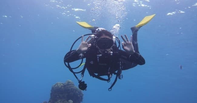 Scuba diver with yellow fins signaling midwater reef dive
