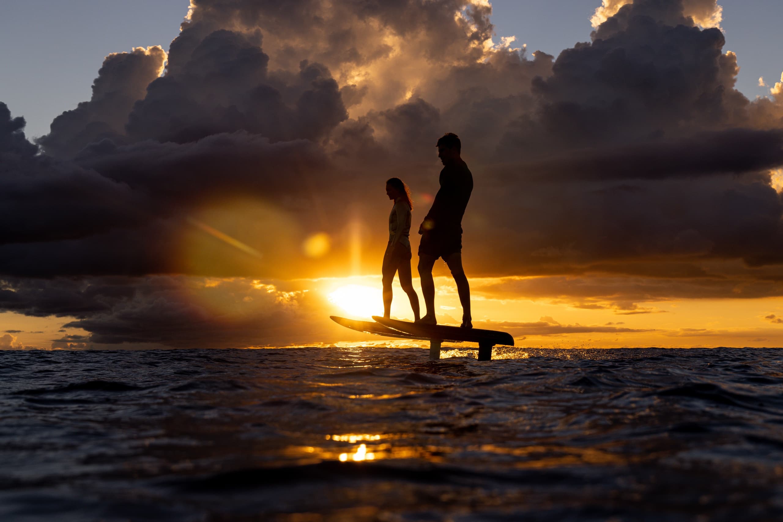 Standup paddleboarders silhouetted at sunset on open ocean