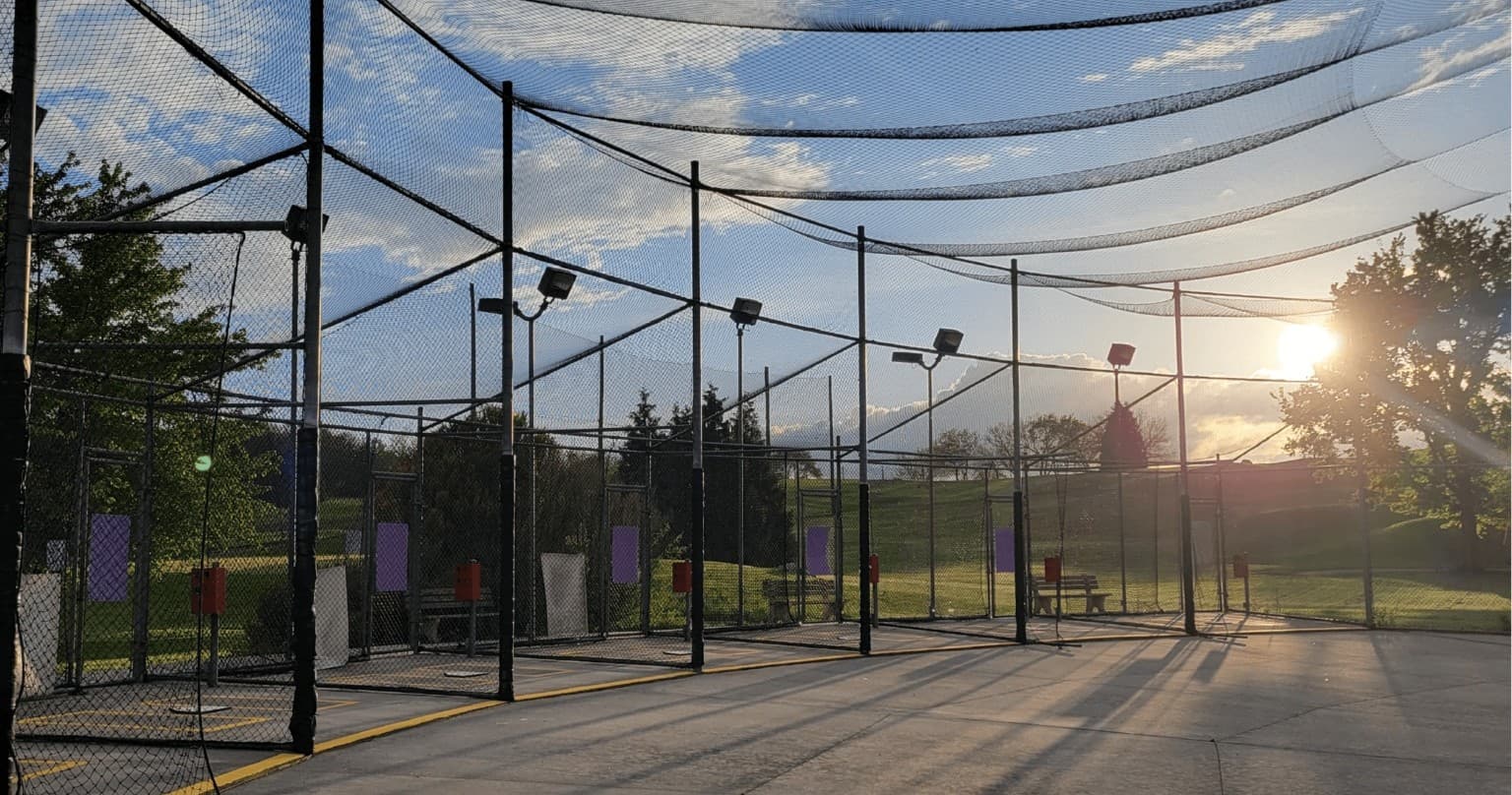 Outdoor batting cages at sunset on fenced practice range