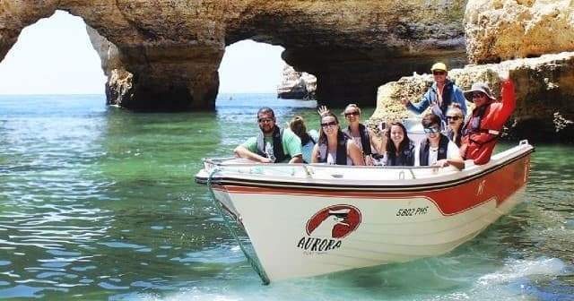 Guided boat tour passing sea arches and cliffs with smiling passengers
