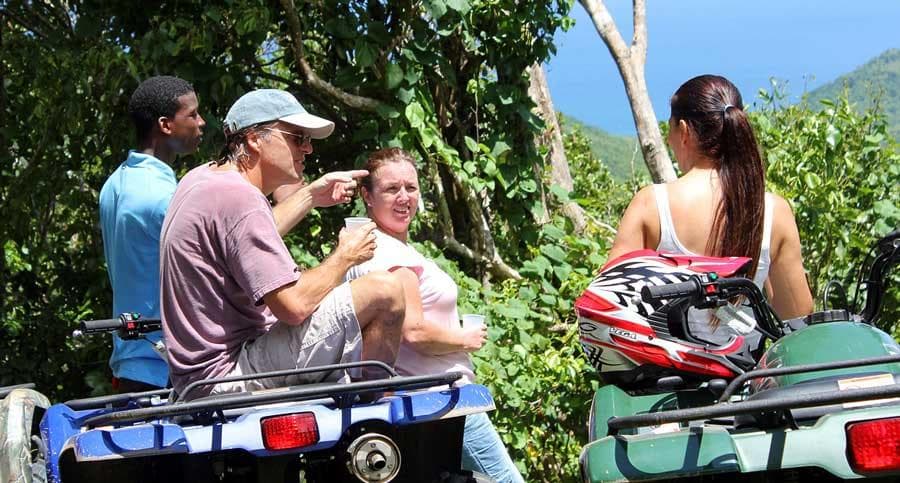 Group of riders chatting beside ATVs on tropical hillside trail