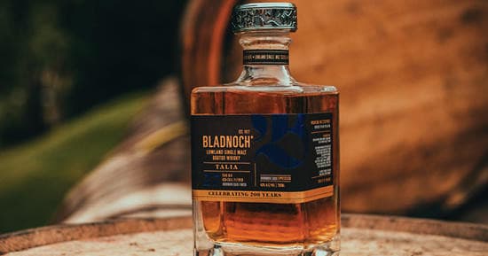 Bladnoch bottle perched on barrel rim with rustic distillery backdrop
