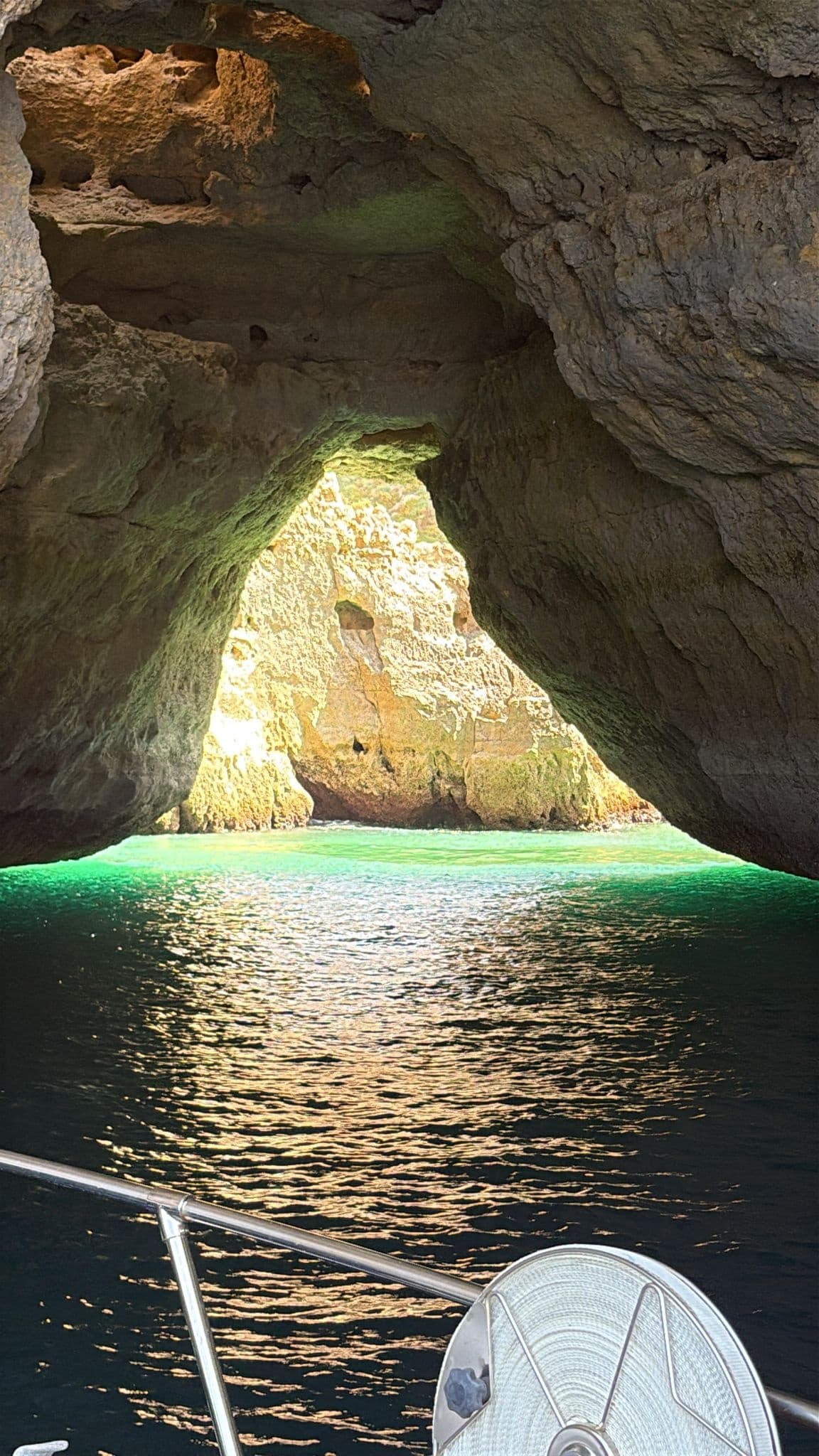 Sunlit Algarve sea cave entrance seen from boat over turquoise water