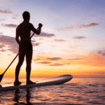 Stand-up paddleboarding at sunset over calm ocean waters