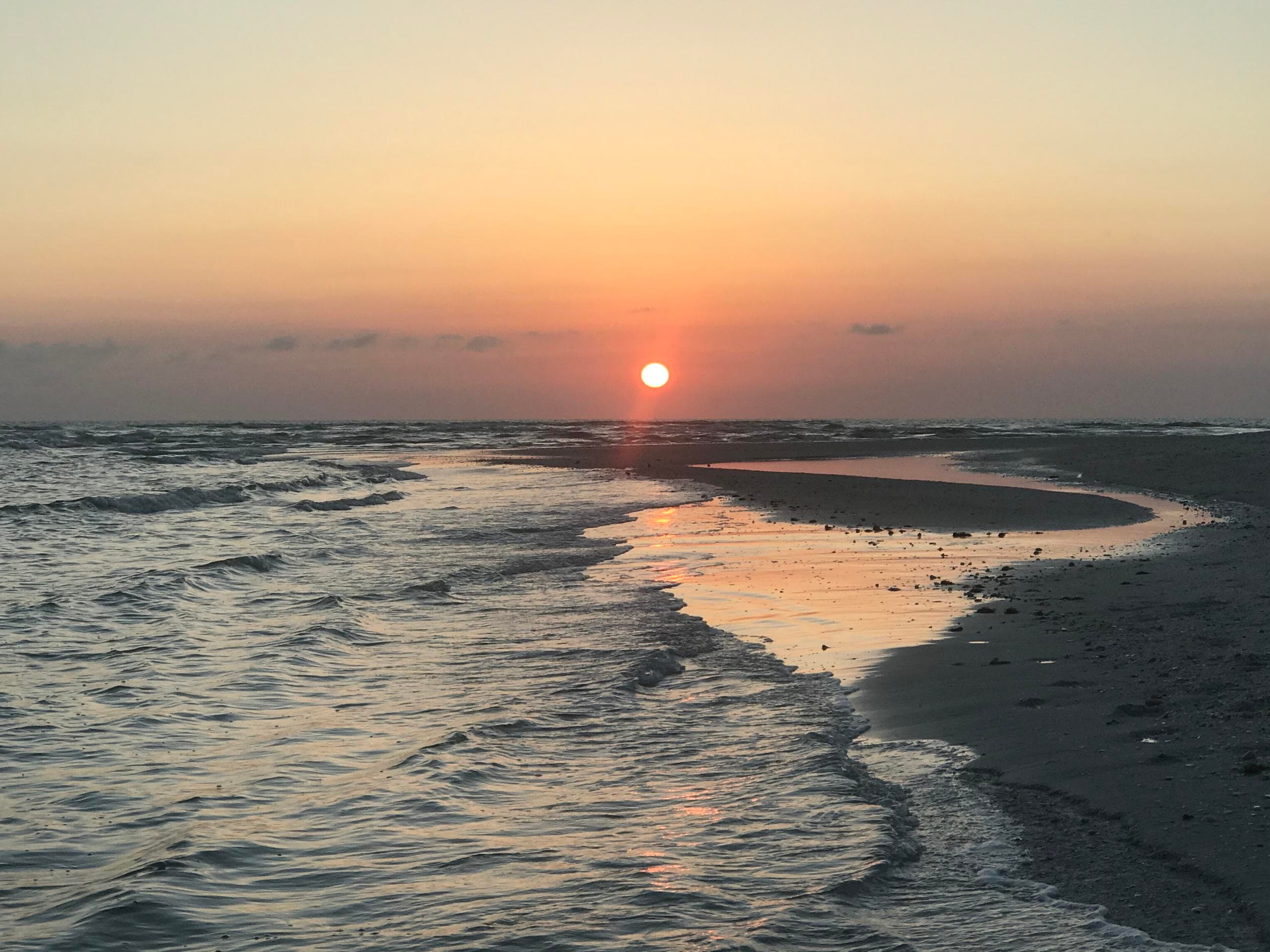 Sunset over coastal beach with curving shoreline and calm waves