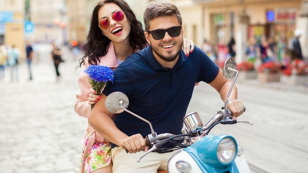 Couple on retro scooter smiling through cobbled city street