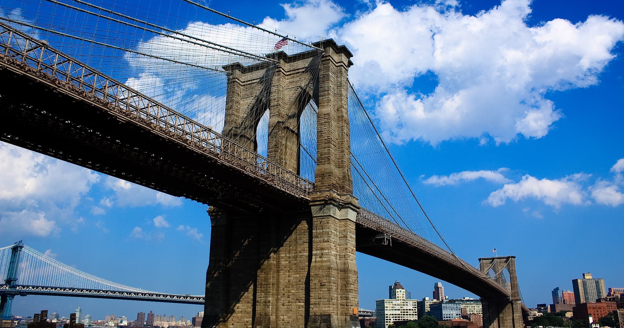 Walking beneath Brooklyn Bridge with clear blue sky above