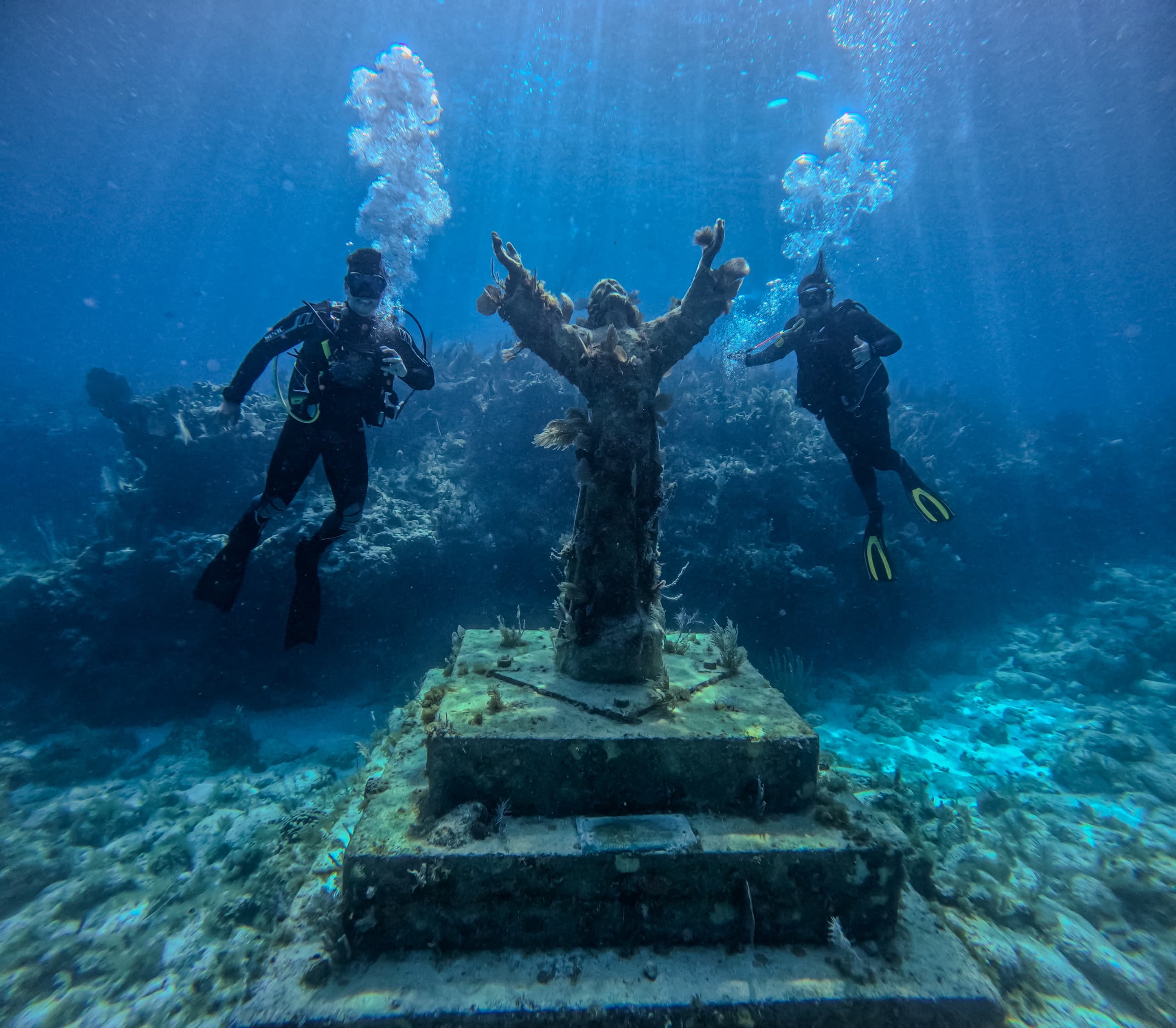 Underwater statue with divers and sunbeams at reef site