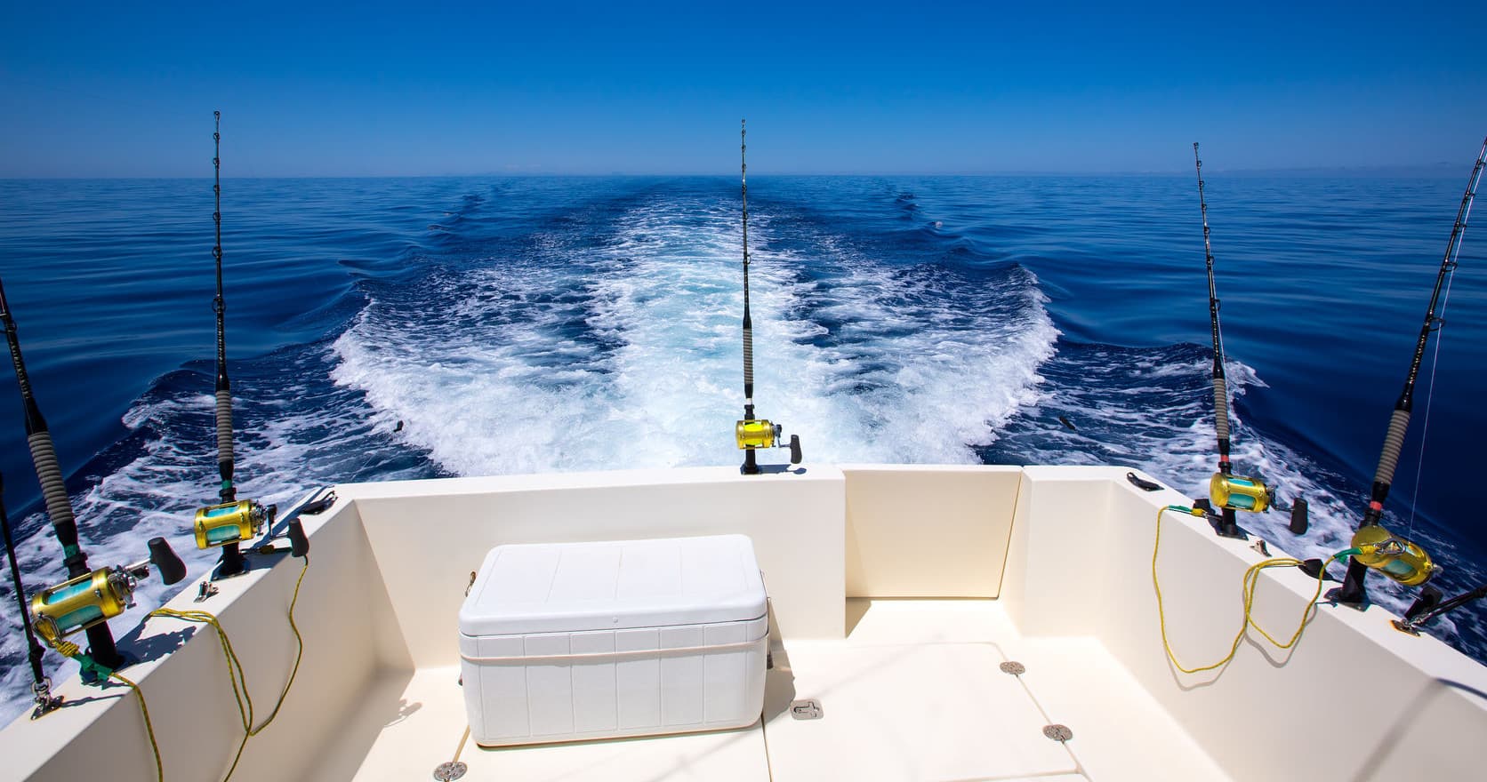 Fishing boat stern showing tackle and wake on deep blue sea